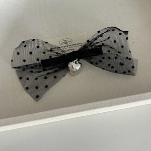 Detail of black mesh polka dot bow hair clip with a silver heart-shaped pendant