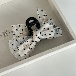 Detailed macro view of an elegant black polka dot mesh bow hair clip on a minimalist display