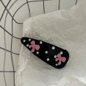 Pink ribbon bow hair clip with black and white polka dots on a metal basket background