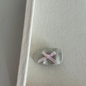 Detail of grey oval hair clip with textured surface and pink ribbon bow on canvas