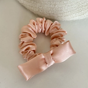 Primer plano de coletero de seda rosa melocotón con brillo satinado y lazo elegante