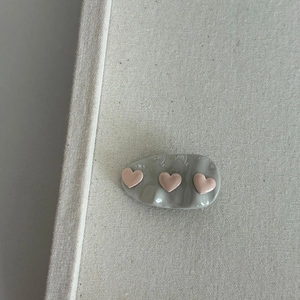 Green wavy hair clip with three pink hearts on a cream canvas background