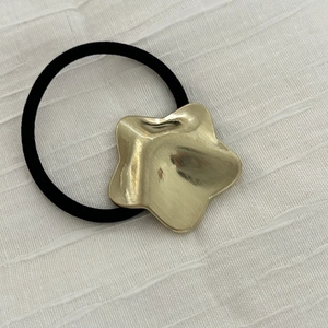 Detail eines goldenen Sternanhängers mit Liquid-Metal-Textur auf schwarzem Haargummi