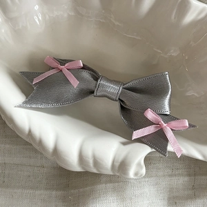 Elegant grey satin bow hair clip with pink ribbon accents on a decorative shell plate