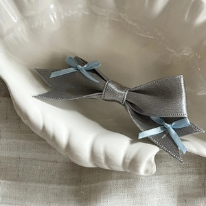 Elegant silver leather bow hair clip with light blue ribbon accents on white ceramic plate