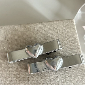 Pair of stylish silver faux leather heart hair clips on a textured beige display background