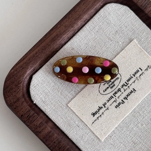 Oval tortoiseshell hair clip with colorful polka dots on a linen background texture
