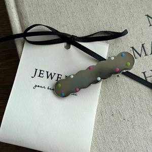 Detailed macro view of a silver wavy hair clip with colorful dots on a display card