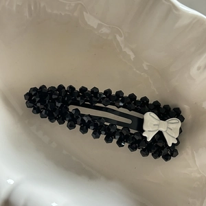 Détail d'une pince à cheveux à perles noires avec un petit nœud blanc élégant