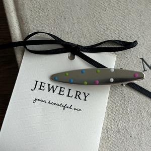 Close-up of a silver hair clip with colorful polka dots on a white jewelry card