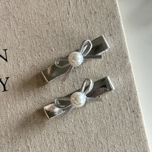 Close-up of two silver bow hair clips with faux pearl center and metal duckbill base