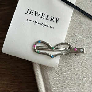 Macro detail of silver heart hair clip with colorful enamel dots on textured card