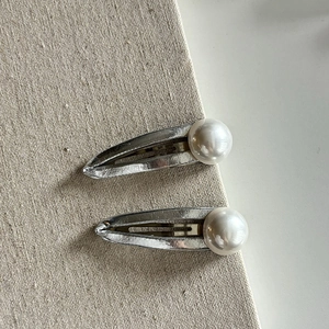 Detail of silver drop hair clips featuring round white pearls on a soft fabric backdrop