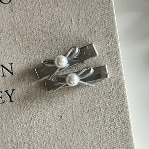 Detail of two silver bow hair clips with white pearls on a grey textured surface