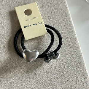 Close-up of black elastic hair ties with silver heart and cylinder metal charms on display card
