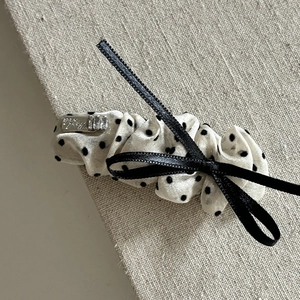 Detailed close-up of cream polka dot bow hair clip with silver logo on fabric surface