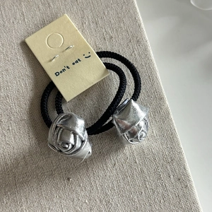 Close-up of two silver fabric rose charms on black elastic hair ties set in beige canvas