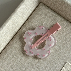Detail of a matte pink flower hair clip featuring delicate rose patterns on a beige texture