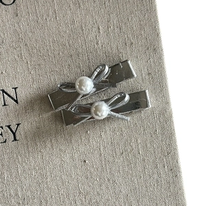Elegant silver metallic bow hair clips with white pearls on a minimalist linen texture