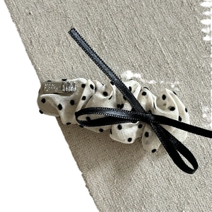 Chic beige polka dot bow hair clip with black ribbon and metallic logo detail