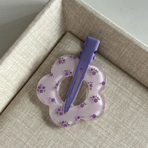 Detailed macro view of purple floral acrylic hair clip on a beige textured tray