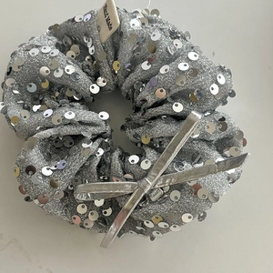 Macro detail of silver sequin scrunchie with a bow and Hand Made woven label
