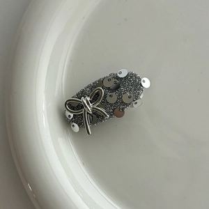 Macro shot of silver glitter hair clip with sequins and a 3D metallic bow on white ceramic