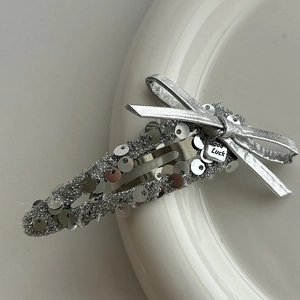 Detail of silver sequin bow hair clip with Good Luck pendant on white ceramic dish