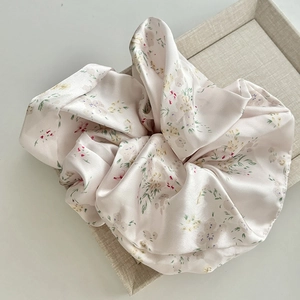 Detail of light pink floral satin scrunchie with soft fabric texture on linen tray