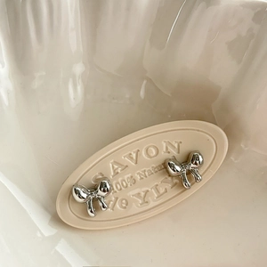 Detailed view of silver bow-shaped stud earrings on a textured cream tray and ceramic bowl