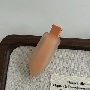 Macro detail of the orange resin hair clip showing smooth texture and metal duckbill grip