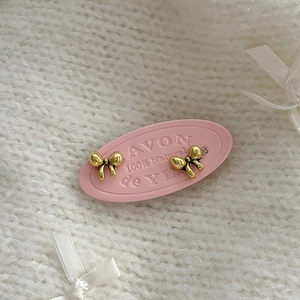 Close-up of golden bow-shaped stud earrings on pink display card with knit background