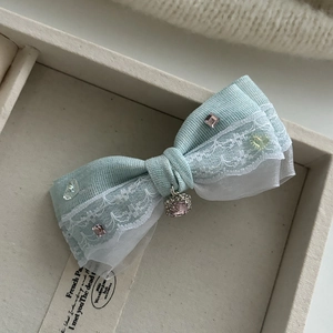 Détail d'une pince à cheveux nœud bleu avec bordure en dentelle et pierres roses