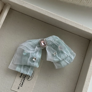 Détail d'une pince à cheveux en dentelle vert clair avec strass rose et ailes papillon