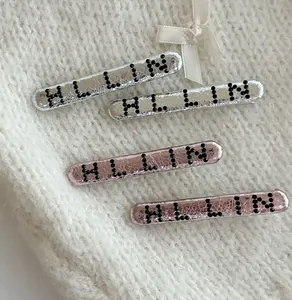 Détail de barrettes argentées et roses avec lettres HLLIN sur fond en maille douce