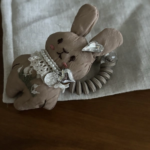 Detail of a brown fabric bunny hair tie with embroidery and heart-shaped metal pendant