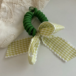 Detailed macro view of green coil hair tie with checkered bow and acrylic pearl bead