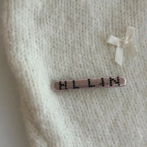 Barrette en métal rose avec inscription HLLIN en strass noirs sur fond tricot blanc