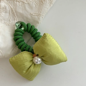 Detail view of a green telephone wire hair tie with satin bow and pearl accent