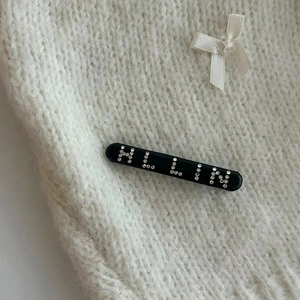 Gros plan sur la barrette noire avec lettres HLLIN en strass brillants sur du tricot