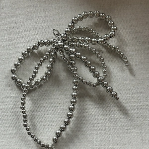 Bijou de chaussure nœud en perles argentées avec pampilles sur fond en tissu texturé