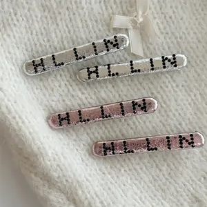 Barrettes à lettres argentées et roses avec strass sur fond de chandail en maille blanc