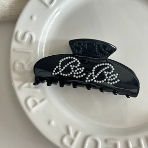 Elegant black acetate hair claw with silver bead Be Be lettering design on ceramic dish