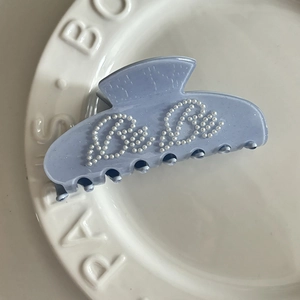 Close-up of light blue acetate hair claw clip with elegant white pearl letter inlay