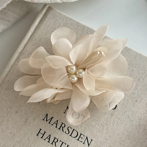 Elegant beige mesh flower hair claw clip with faux pearls on a vintage linen book background
