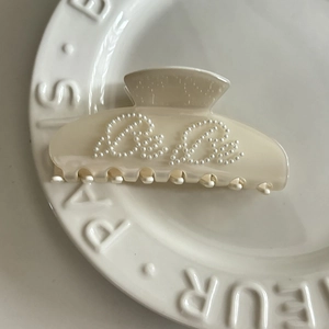 Detail view of cream acetate hair claw clip featuring Bebe pearl letter embellishments
