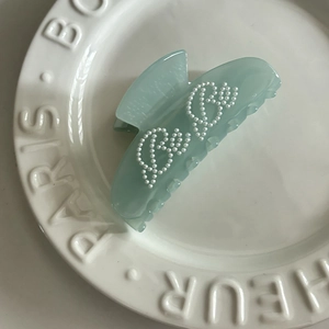 Detail view of a mint green translucent acetate hair claw clip with pearl letter patterns