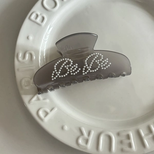 Detail of grey acetate hair claw with white pearl BeBe lettering on a ceramic plate
