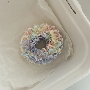 Dettaglio di un elastico per capelli all'uncinetto color pastello in un contenitore bianco
