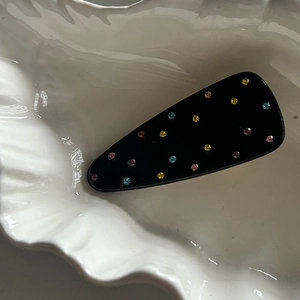 Macro shot of a black triangular hair clip with colorful rhinestones on white ceramic